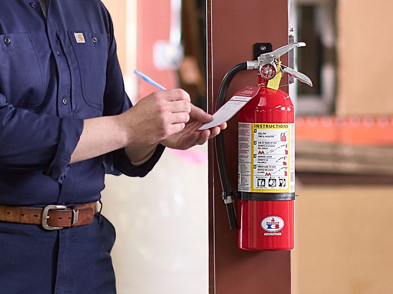 Technician inspecting and tagging a wall-mounted fire extinguisher